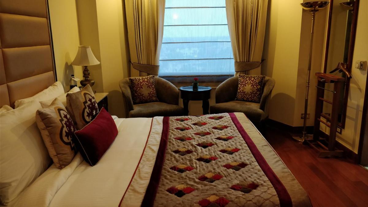 a bedroom with a bed and two chairs and a window at Jaypee Vasant Continental in New Delhi