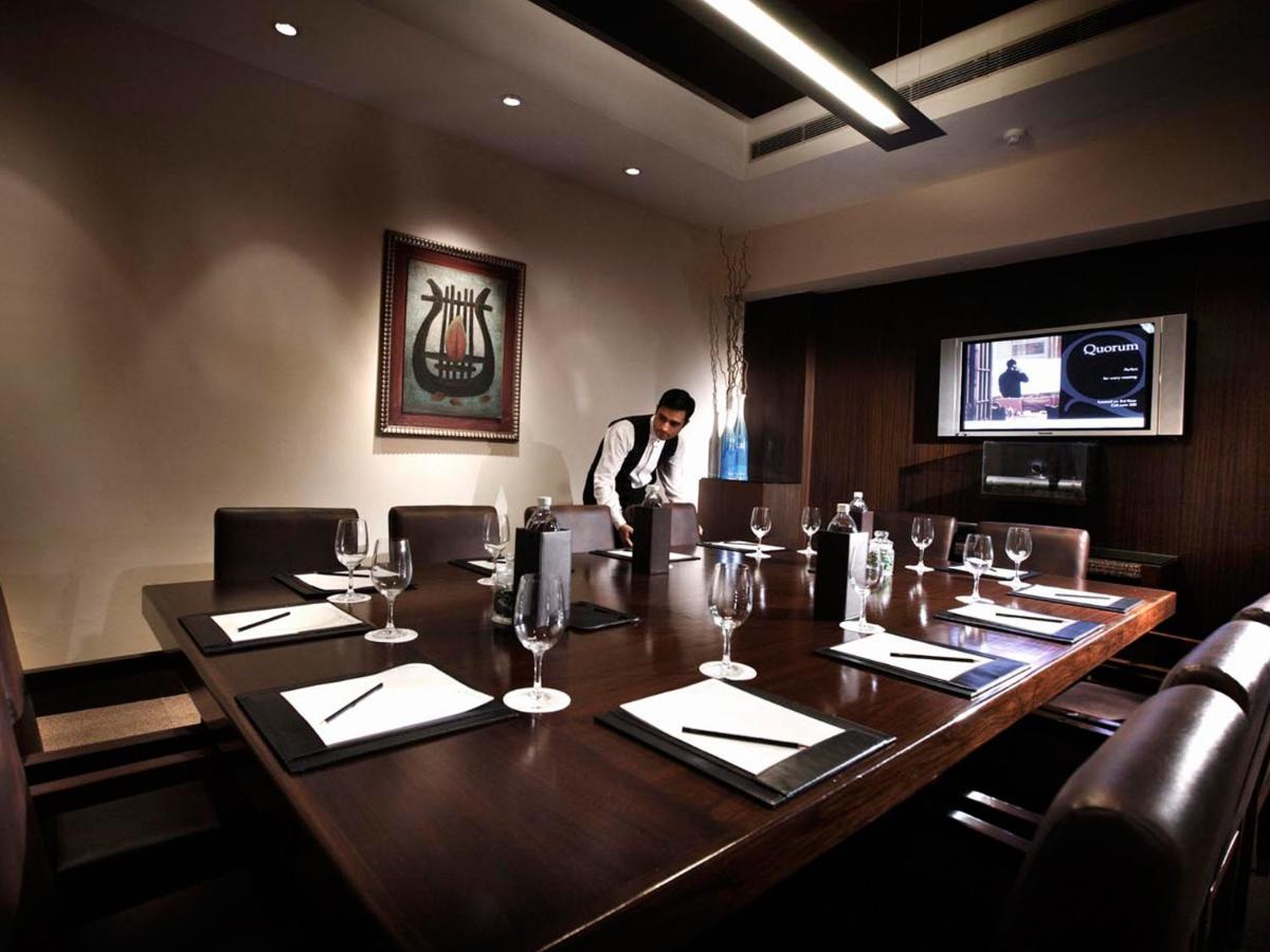 a man standing behind a large wooden table in a restaurant at The LaLiT New Delhi in New Delhi