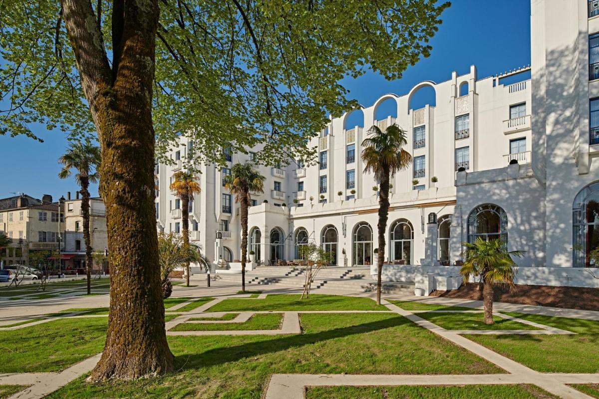 un grand bâtiment blanc avec des palmiers devant dans l'établissement Hotel & Spa Vacances Bleues Le Splendid, à Dax