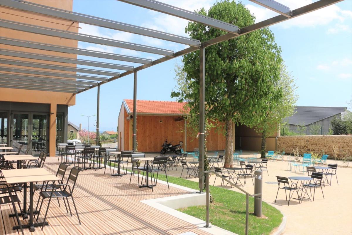 un patio avec des tables et des chaises en face d'un bâtiment dans l'établissement Le Felicien, à Saint-Félicien