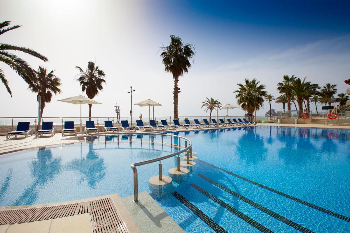 Una gran piscina con sillas y palmeras. en Hotel & Spa Peñiscola Palace, en Peñíscola