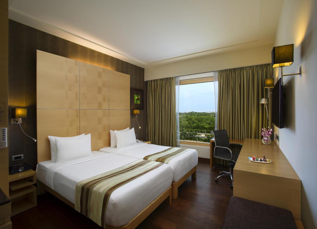 a hotel room with a bed and a desk and a window at Novotel Hyderabad Airport in Hyderabad