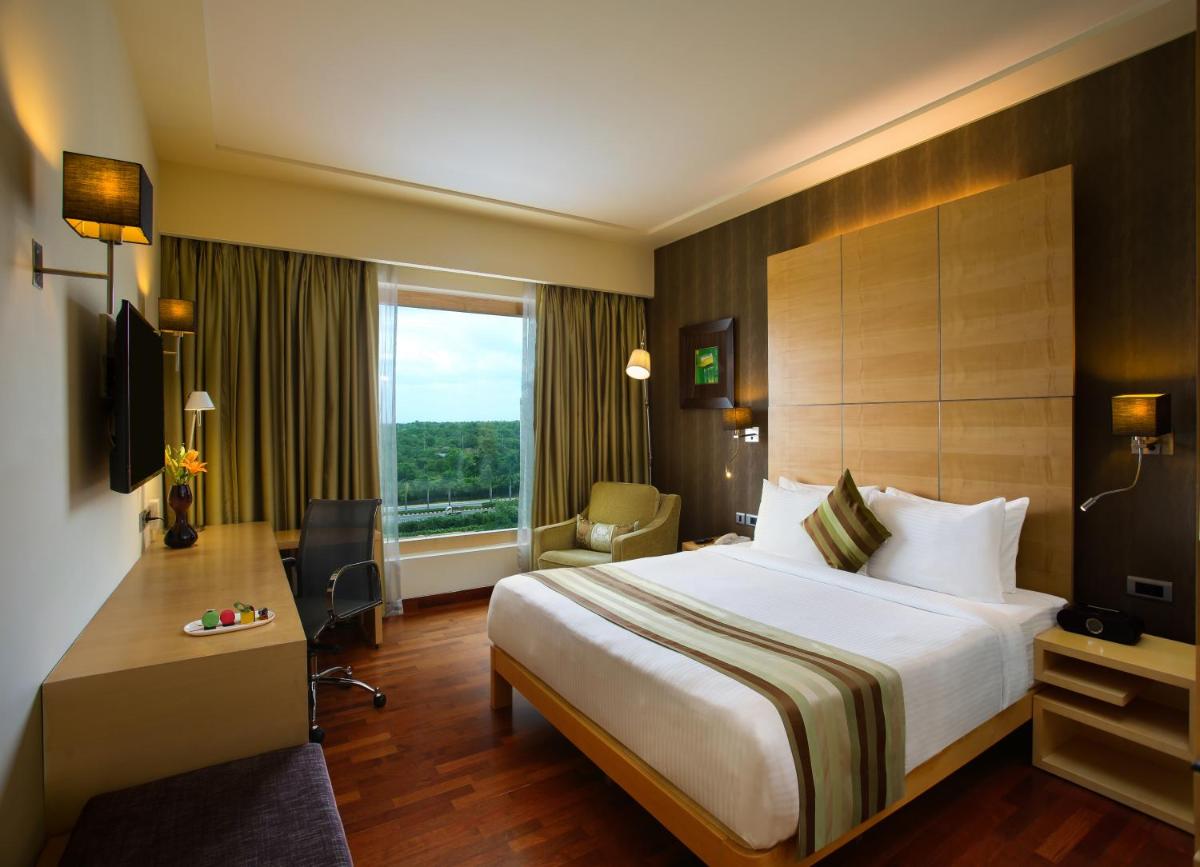 a hotel room with a bed and a desk and a window at Novotel Hyderabad Airport in Hyderabad