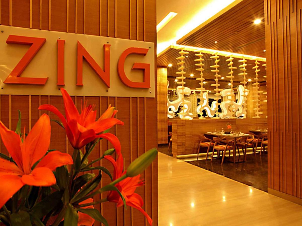 a restaurant with a zing sign on the wall and red flowers at The Metropolitan Hotel & Spa New Delhi in New Delhi