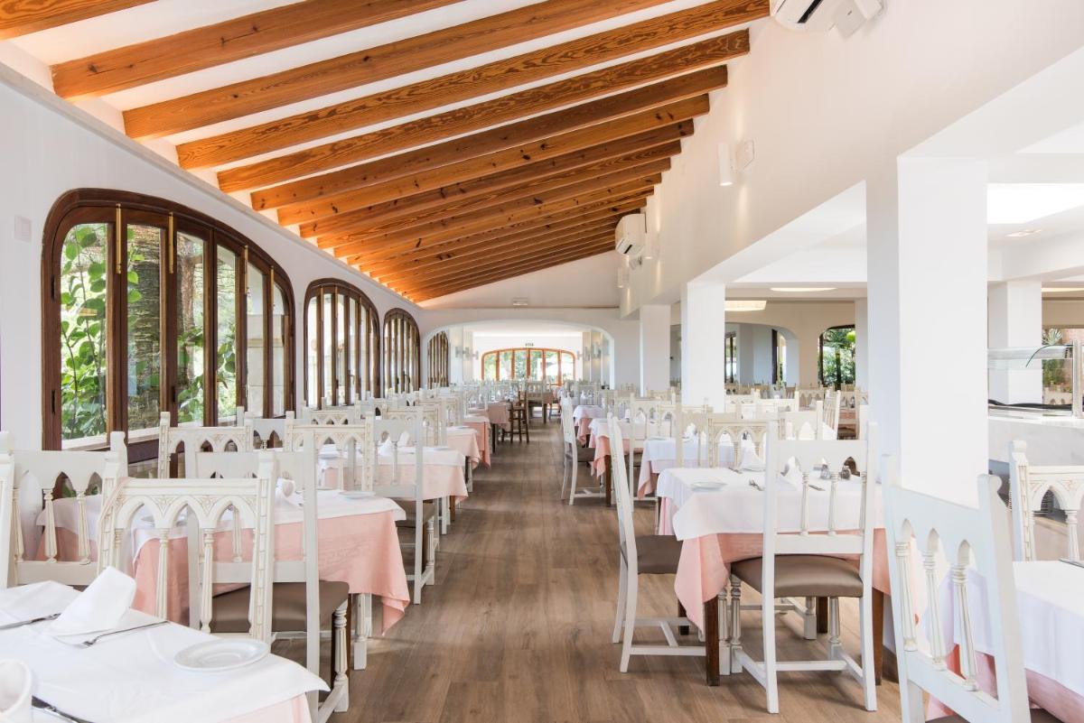 Un comedor con mesas y sillas blancas. en Hotel Na Taconera, en Cala Ratjada