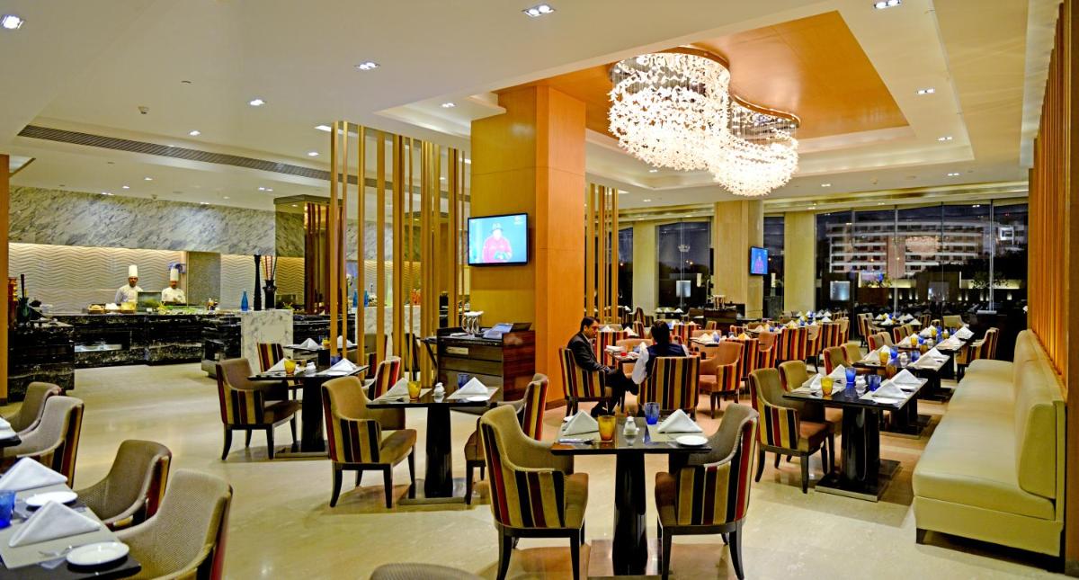 a restaurant with tables and chairs and a chandelier at Radisson Blu Jaipur in Jaipur