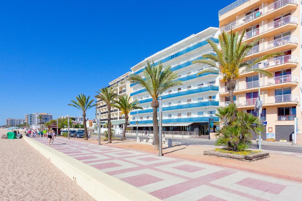 Un edificio en la playa con palmeras y una acera. en Hotel Pimar & Spa, en Blanes