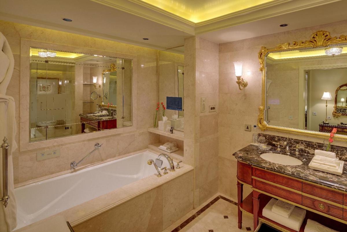 a bathroom with a tub and a sink and a mirror at The Leela Palace New Delhi in New Delhi a bathroom with a tub and a sink and a mirror at The Leela Palace New Delhi in New Delhi