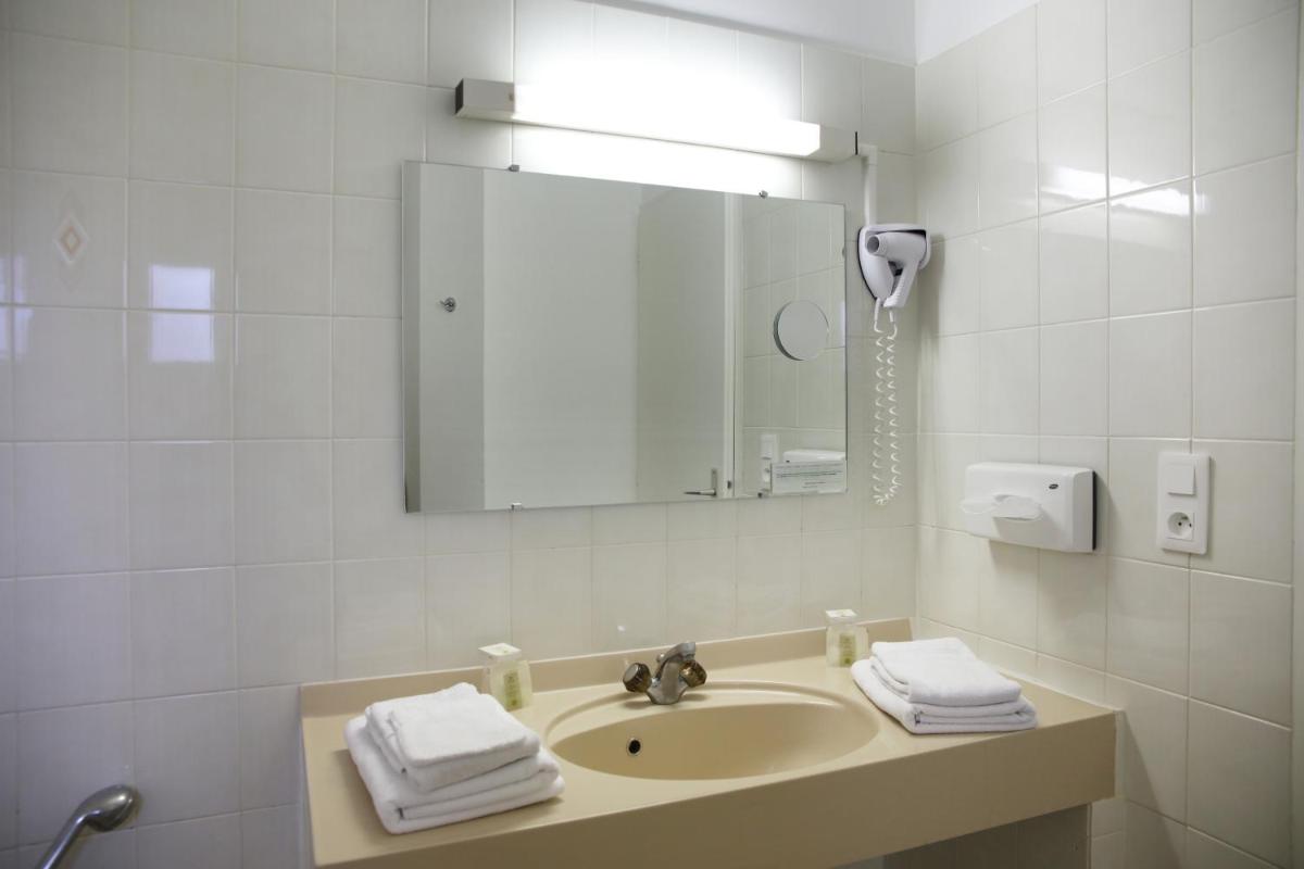 une salle de bains blanche avec un lavabo et un miroir dans l'établissement Logis Hotel Le Nuage, à La Bussière 52 autres photos