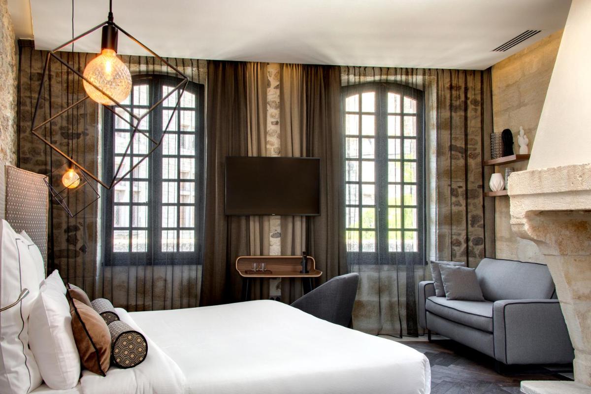 - une chambre avec un lit, une chaise et une télévision dans l'établissement Boutique Hôtel des Remparts & Spa, à Aigues-Mortes