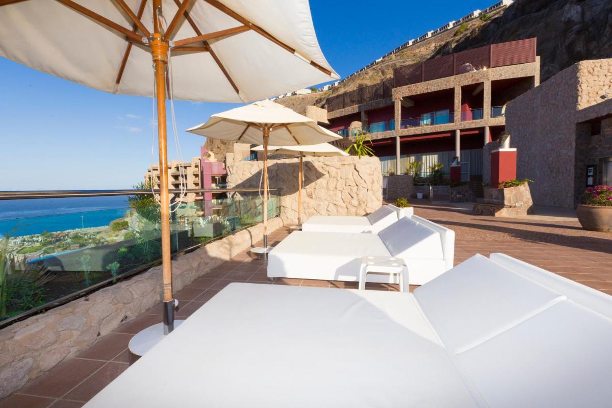 un patio con sombrilla, mesas y sillas blancas en Gloria Palace Royal Hotel & Spa, en Puerto Rico de Gran Canaria
