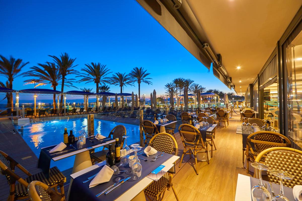 Un restaurante con vistas a la piscina y palmeras. en Hotel Negresco - Adults Only, en Playa de Palma