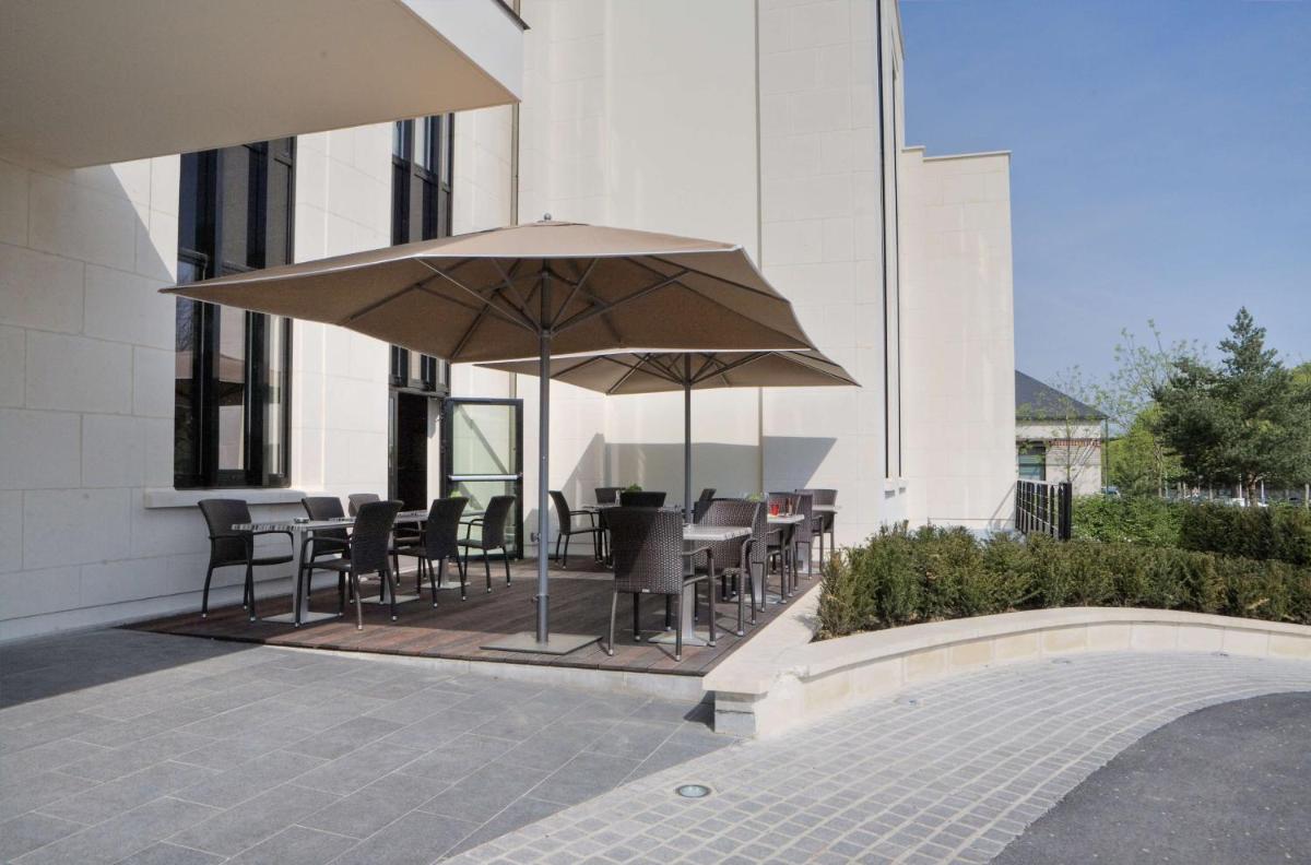 une terrasse avec tables, chaises et parasol dans l'établissement Best Western Plus Hotel des Francs, à Soissons