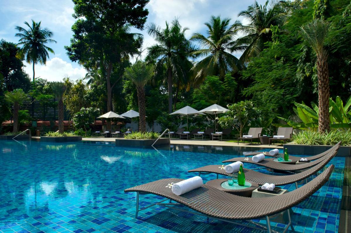 a resort swimming pool with two lounge chairs and trees at Taj Coromandel in Chennai