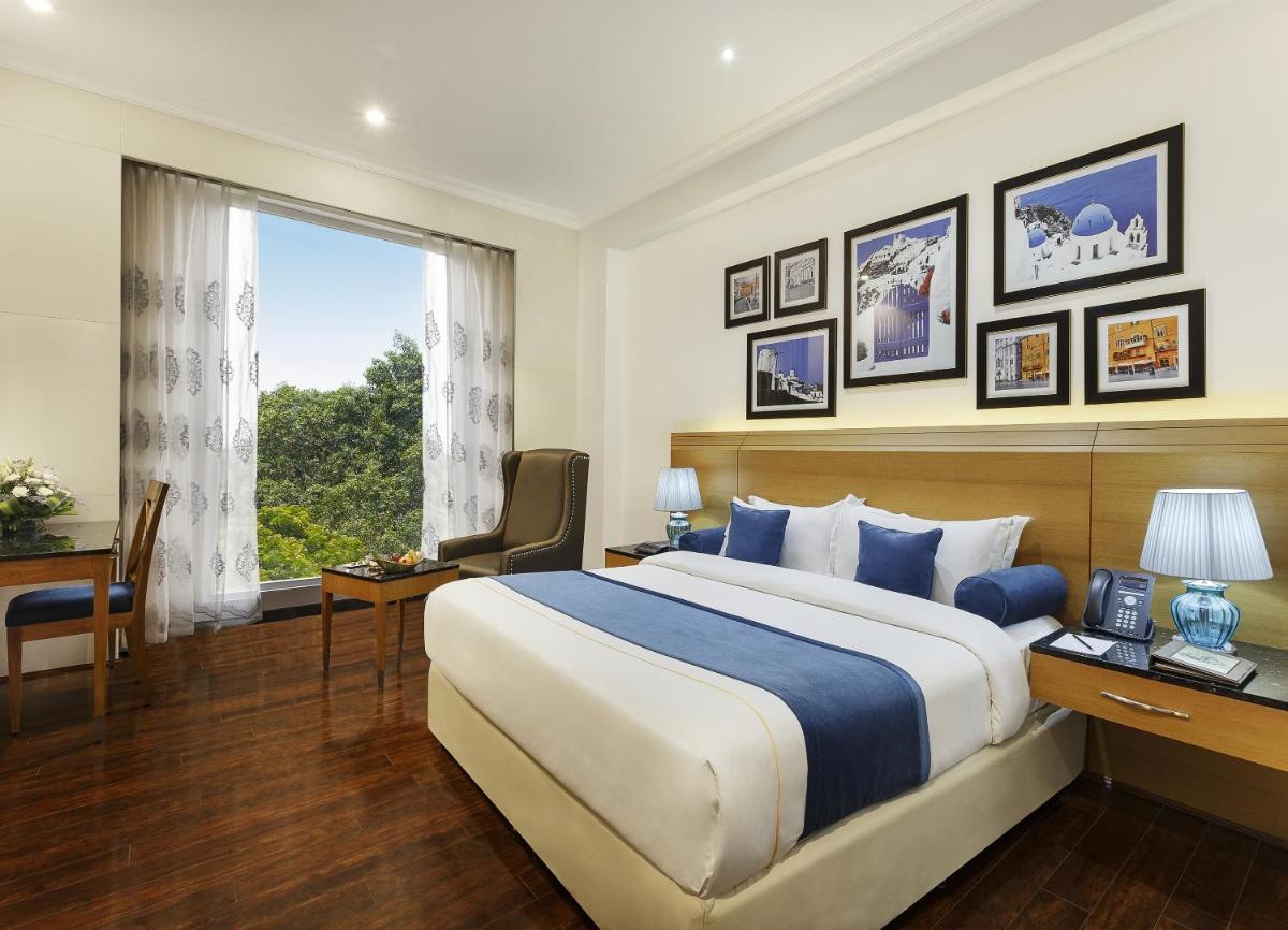 a hotel room with a bed and a desk and a window at La Marvella, Bengaluru in Bengaluru