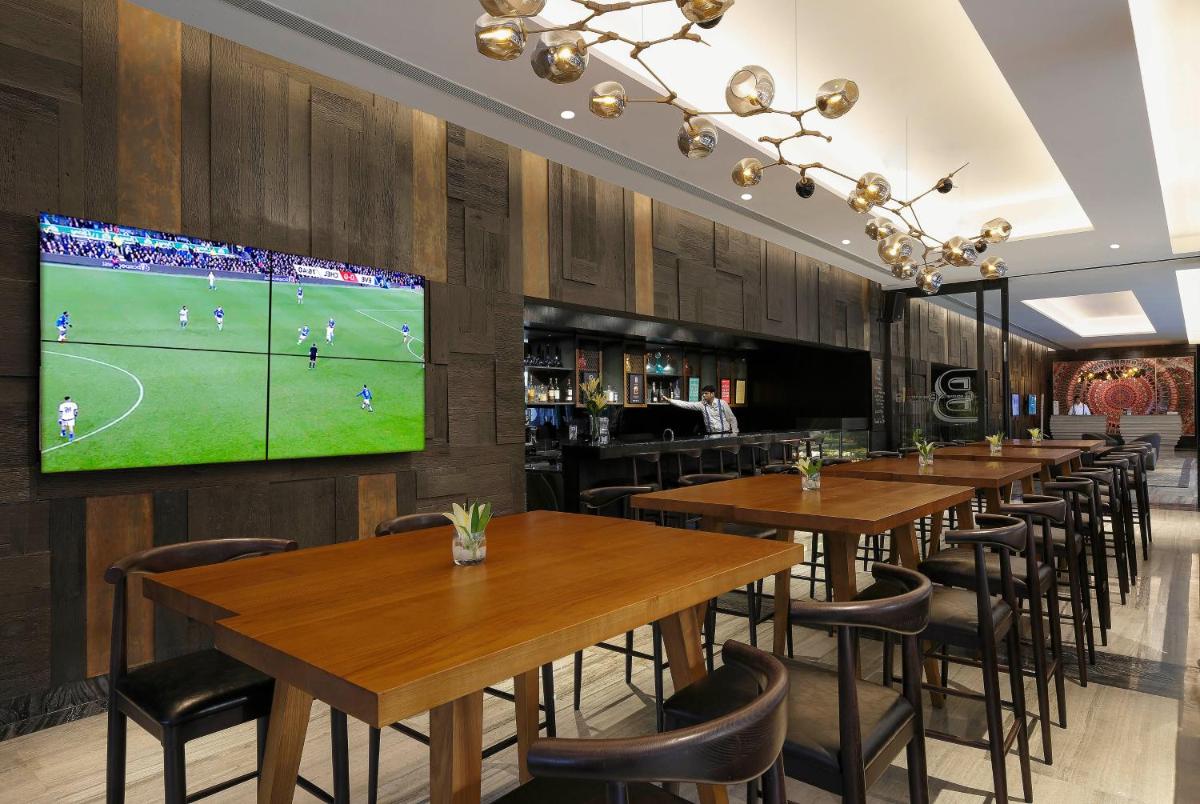 a restaurant with wooden tables and a large tv on the wall at Novotel Chennai Chamiers Road in Chennai
