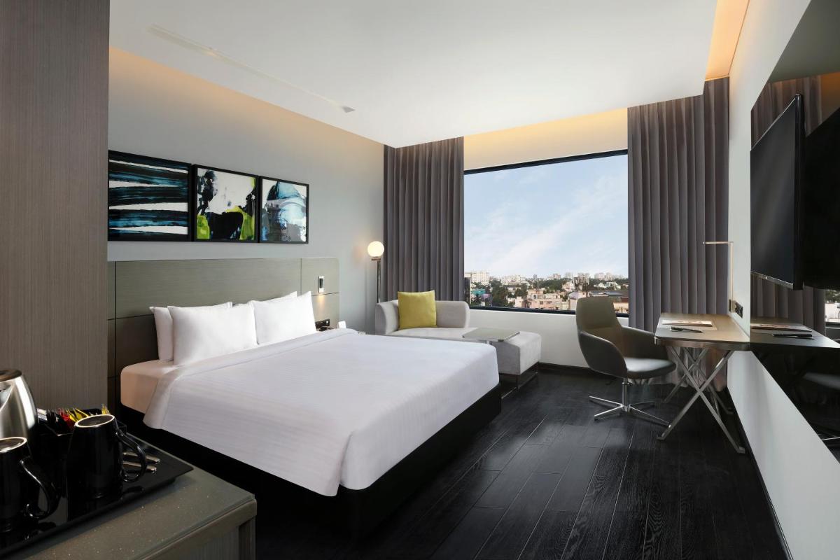 a hotel room with a large white bed and a desk at Novotel Chennai Chamiers Road in Chennai