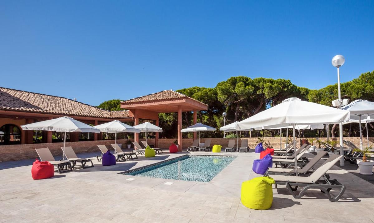 una piscina con sillas y sombrillas junto a un complejo en Barceló Punta Umbría Beach Resort, en Punta Umbría