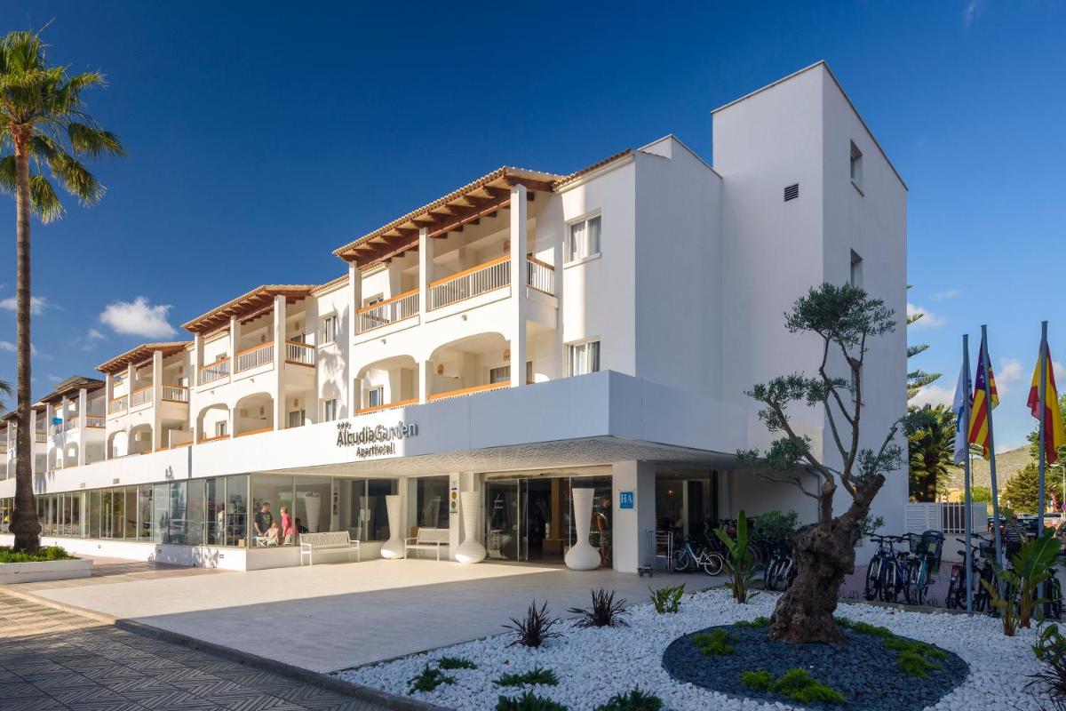 Un gran edificio blanco con palmeras delante. en Alcudia Garden Aparthotel, en Puerto de Alcudia