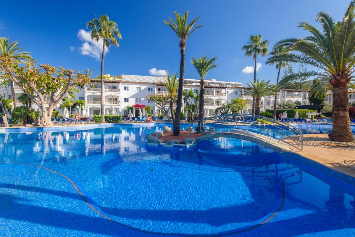 Una gran piscina con palmeras y edificios. en Alcudia Garden Aparthotel, en Puerto de Alcudia