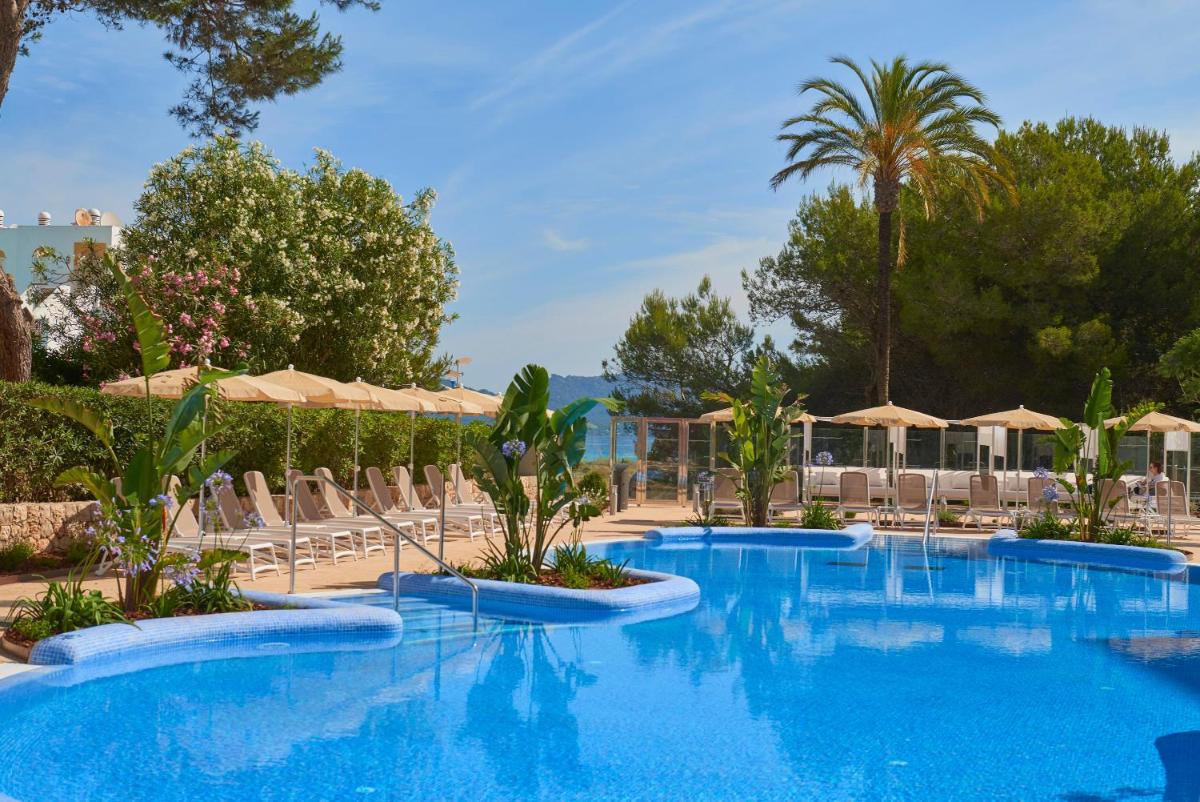 Una piscina con sillas y sombrillas en un resort. en Hipotels Bahia Cala Millor - Adults Only, en Cala Millor