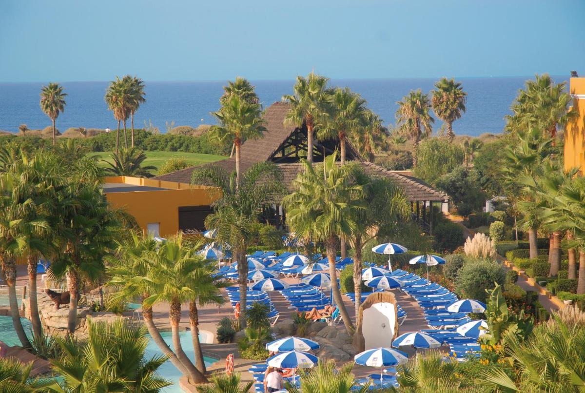 un complejo con sombrillas azules y blancas y palmeras en Playaballena, en Costa Ballena