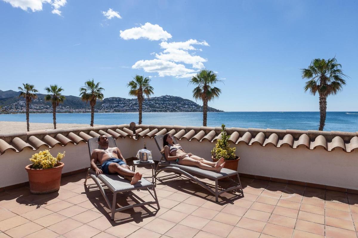 2 personas sentadas en sillas en un balcón con vistas a la playa en Hotel Montecarlo Spa & Wellness, en Roses