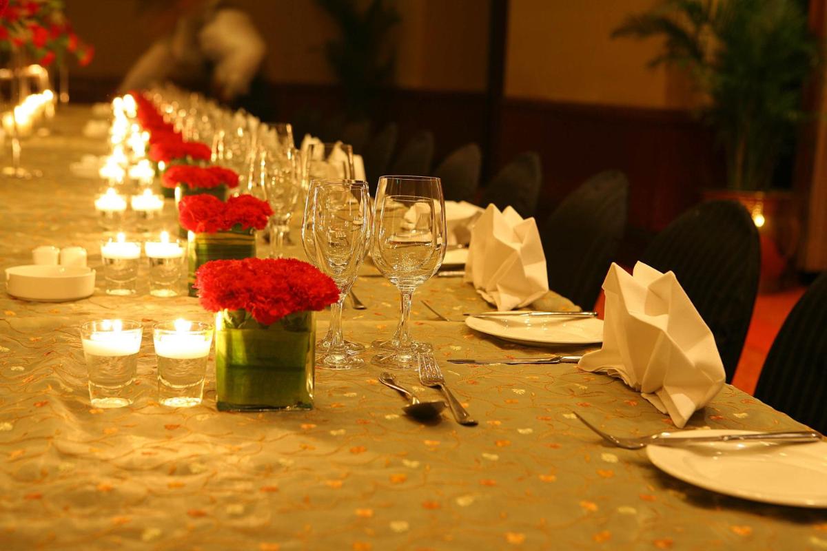 a long table with wine glasses and red flowers on it at Eros Hotel New Delhi, Nehru Place in New Delhi a long table with wine glasses and red flowers on it at Eros Hotel New Delhi, Nehru Place in New Delhi