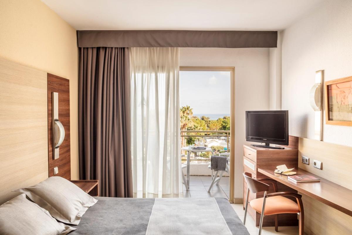 Una habitación de hotel con una cama y un escritorio con televisión. en AQUA Hotel Aquamarina & Spa, en Santa Susanna
