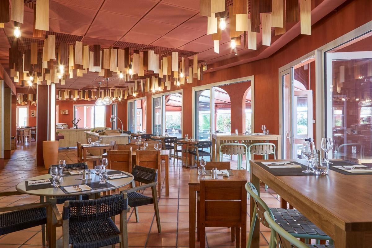 un restaurant avec des tables et des chaises en bois et des lustres dans l'établissement ibis Thalassa Hyeres Plage, à Hyères