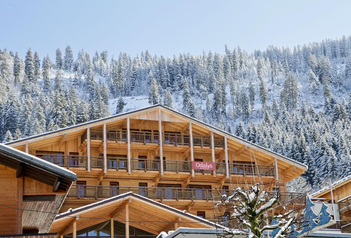 un grand bâtiment en bois avec des arbres enneigés dans l'établissement Résidence Odalys Les Fermes de Châtel, à Châtel