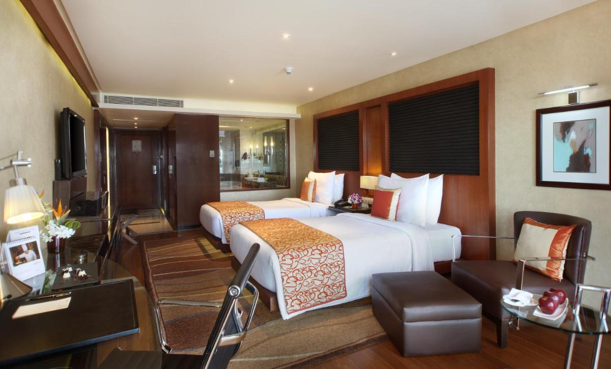 a hotel room with two beds and a couch at Gokulam Grand Hotel & Spa Bangalore in Bengaluru a hotel room with two beds and a couch at Gokulam Grand Hotel & Spa Bangalore in Bengaluru