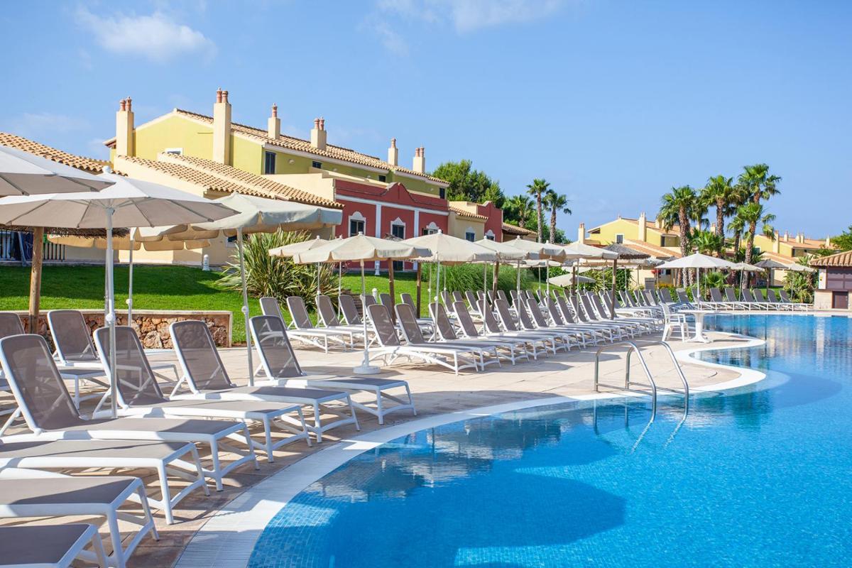 Una fila de sillas y sombrillas junto a una piscina. en Grupotel Playa Club, en Son Xoriguer
