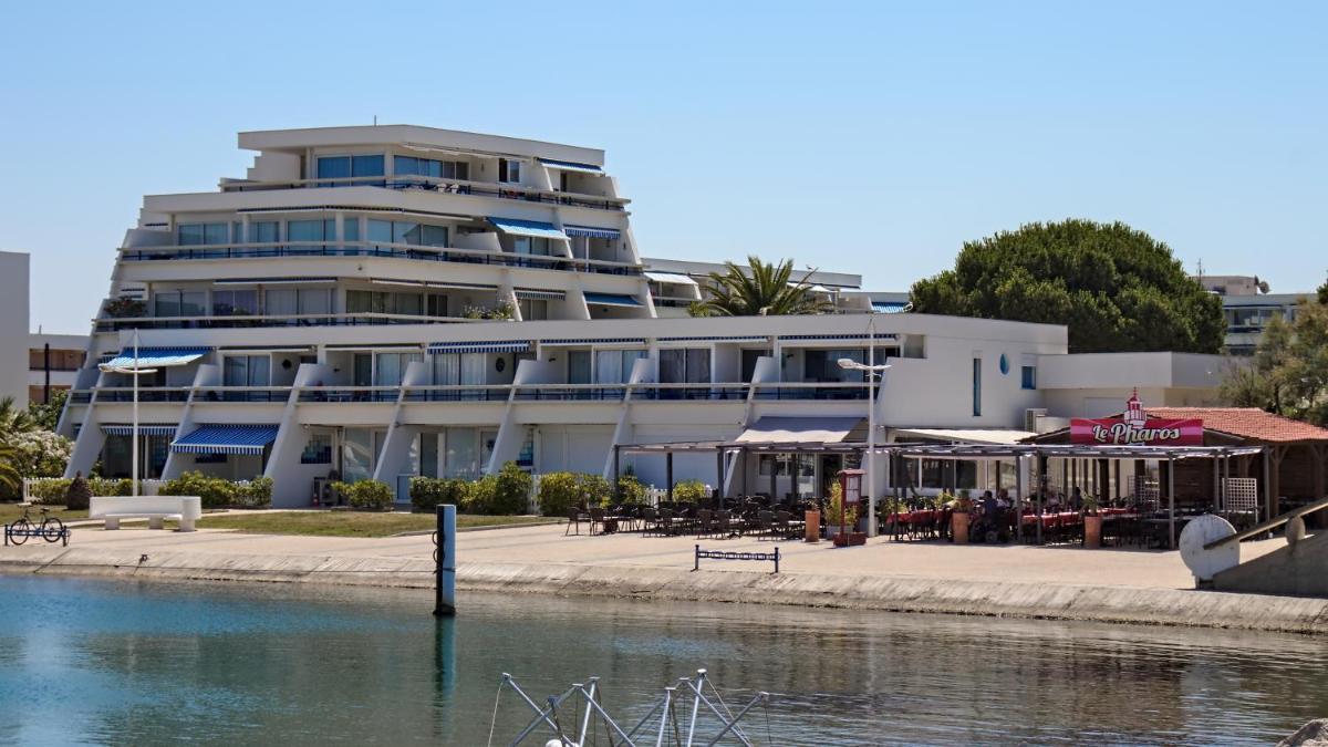 un bâtiment avec des tables et des parasols au bord d'un plan d'eau dans l'établissement Rivages d'Ulysse Port Camargue, au Grau-du-Roi