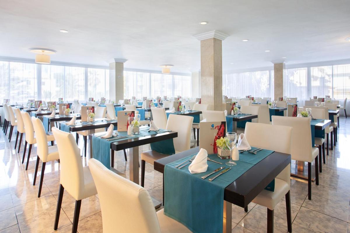 Un comedor con mesas y sillas y ventanas. en Grupotel Montecarlo, en Can Picafort