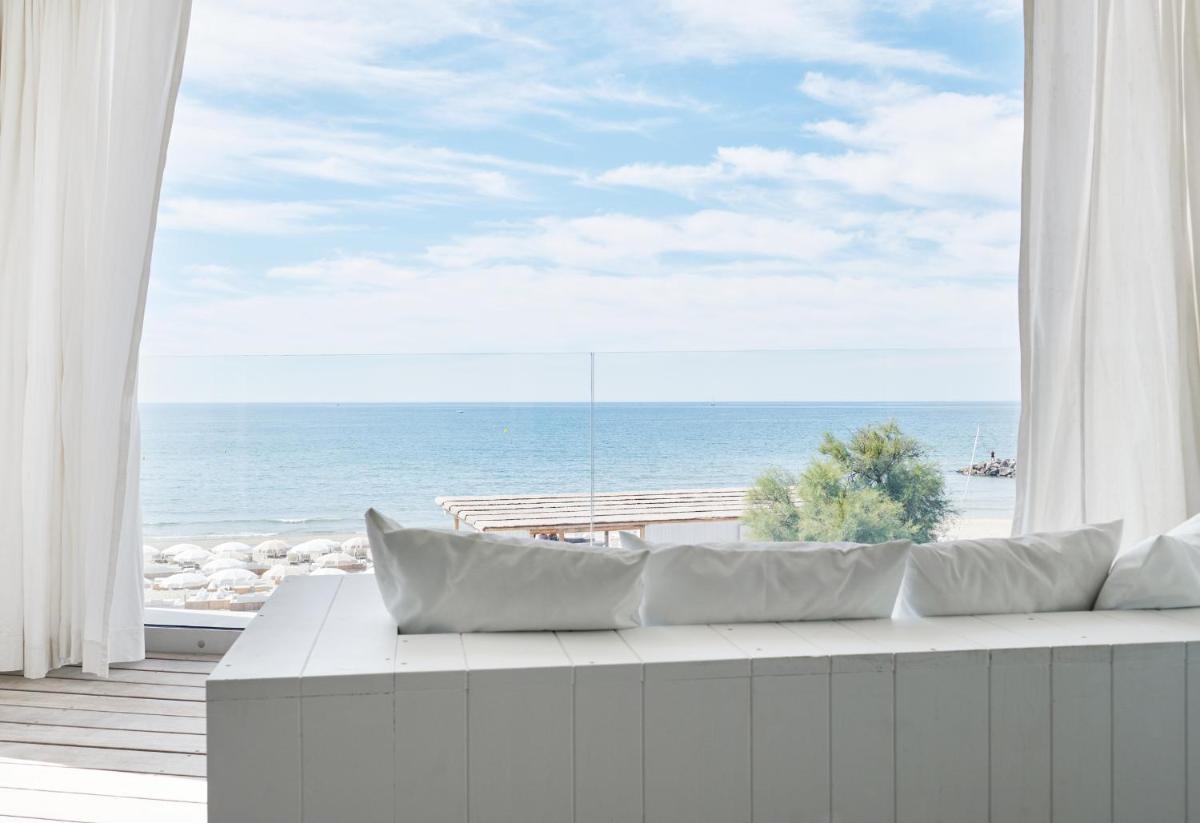un canapé blanc devant une fenêtre avec l'océan dans l'établissement Hôtel Plage Palace & Spa, à Palavas-les-Flots