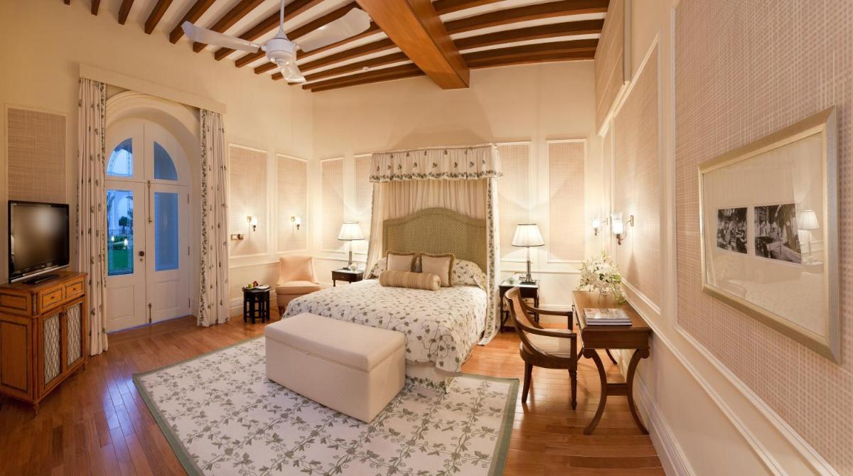 a bedroom with a bed and a desk and a tv at Taj Falaknuma Palace in Hyderabad