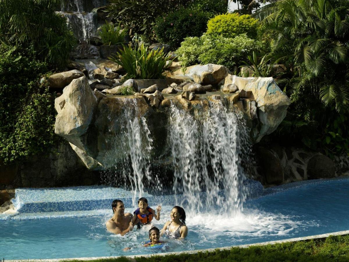 a group of people swimming in a pool with a waterfall at The Retreat Hotel & Convention Centre in Mumbai