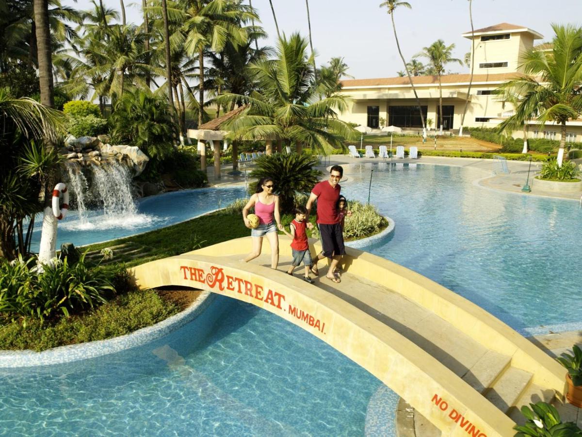 a family walking over a bridge over a pool at a resort at The Retreat Hotel & Convention Centre in Mumbai