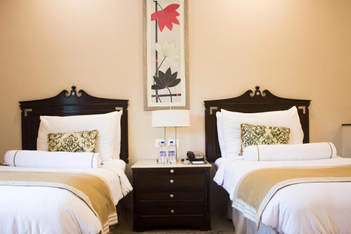 a bedroom with two beds and a table with a lamp at The Claridges New Delhi in New Delhi a bedroom with two beds and a table with a lamp at The Claridges New Delhi in New Delhi