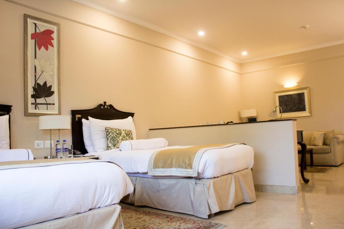 a hotel room with two beds and a chair at The Claridges New Delhi in New Delhi a hotel room with two beds and a chair at The Claridges New Delhi in New Delhi