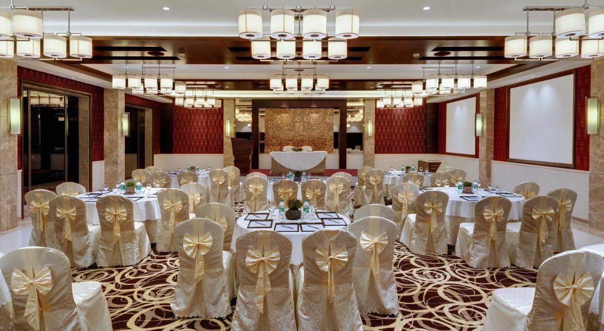 a banquet hall with white tables and chairs and chandeliers at The Fern Kadamba Hotel And Spa in Old Goa
