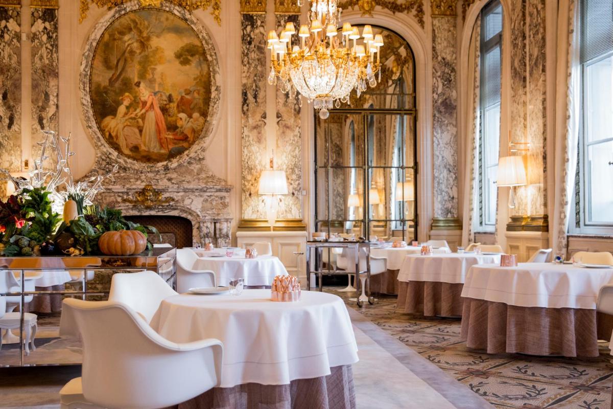 une salle à manger avec des tables et un lustre dans l'établissement Le Meurice – Dorchester Collection, à Paris