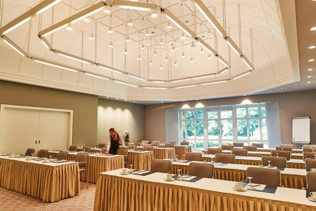 eine Frau steht in einem großen Raum mit Tischen und Stühlen in der Unterkunft Steigenberger ICON Grandhotel & Spa Petersberg in Königswinter + 37 Fotos