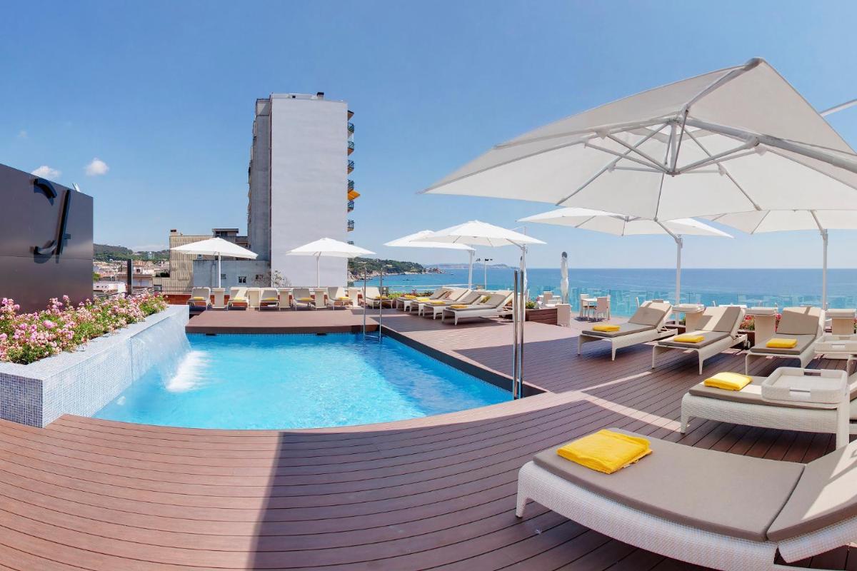 Una piscina con sillas y sombrillas en una terraza. en Cosmopolita Hotel Boutique & Spa, en Platja d'Aro