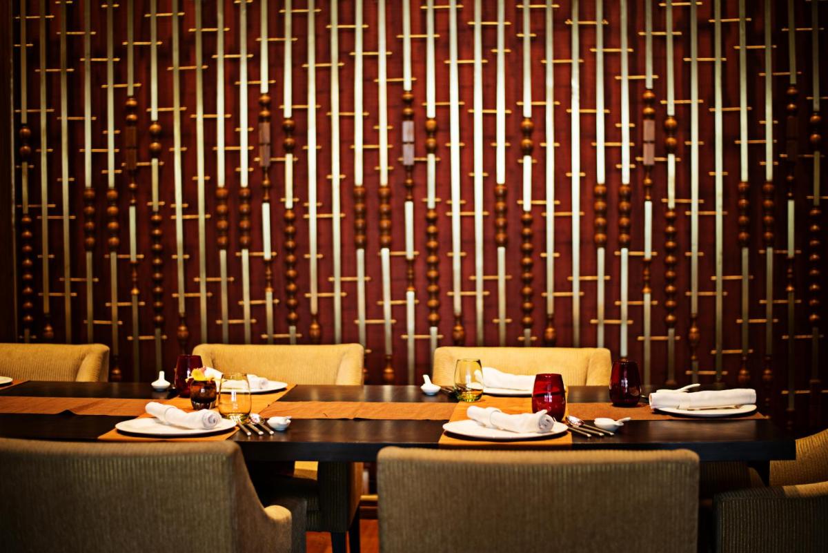 a dining room with two tables and chairs and a wall at Taj City Centre Gurugram in Gurgaon