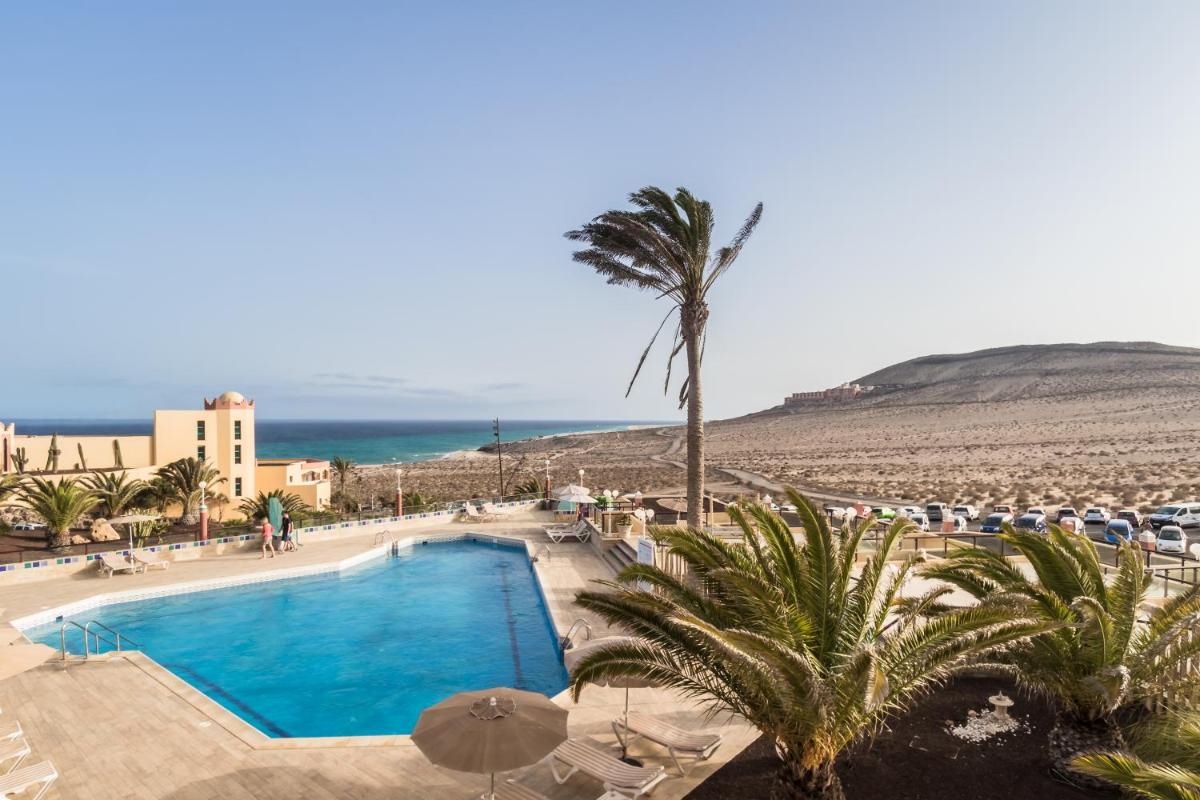 una piscina con una palmera y una playa en Hotel Esmeralda Maris by LIVVO, en Costa Calma