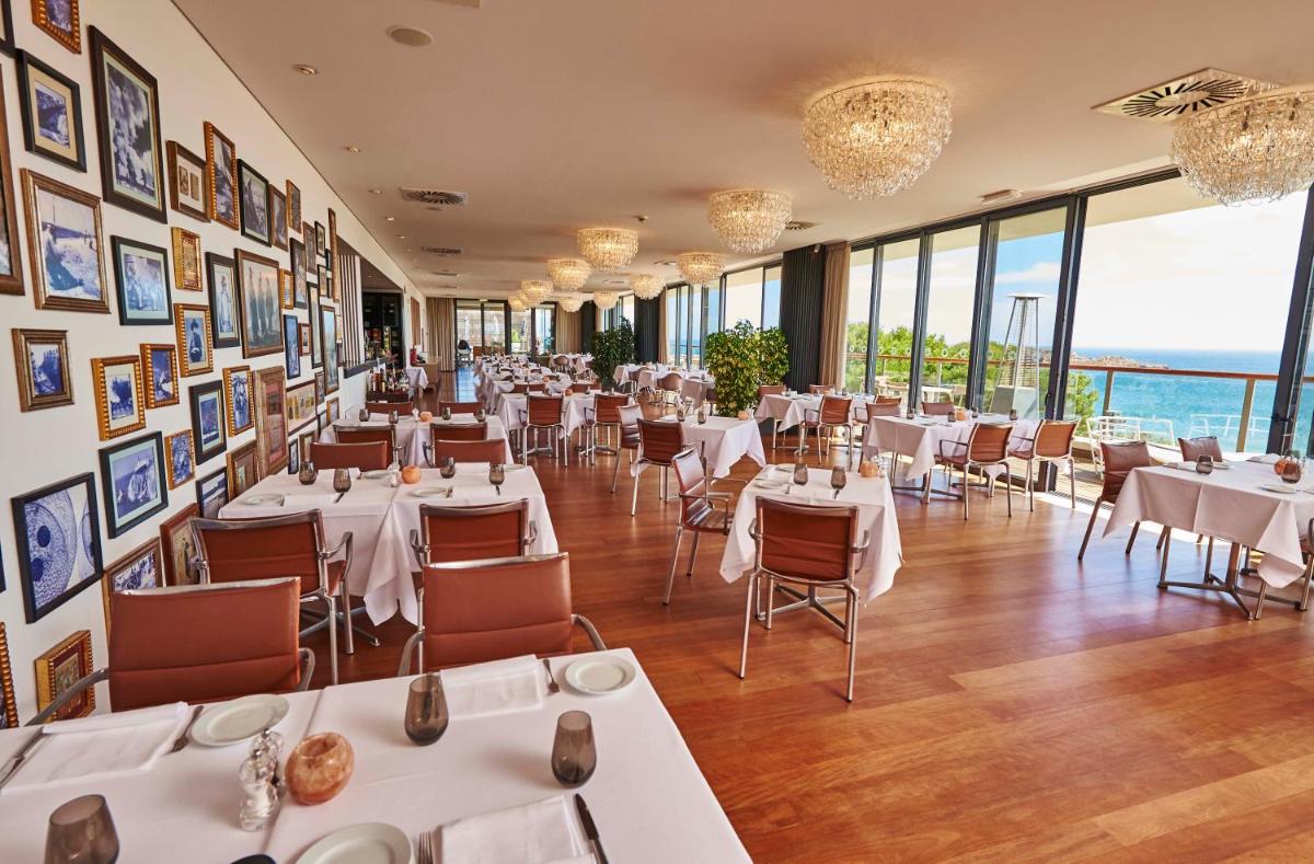 um restaurante com mesas, cadeiras e janelas brancas em Martinhal Sagres Beach Family Resort Hotel em Sagres