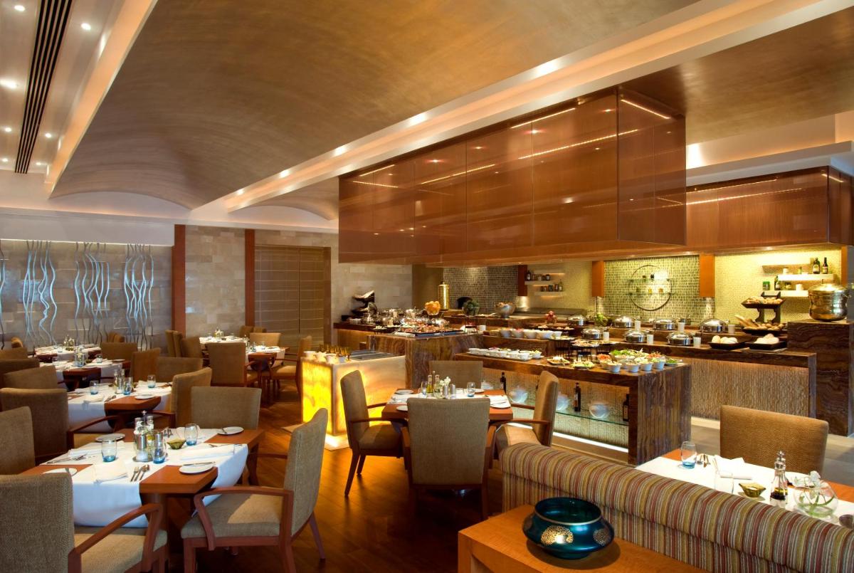 a restaurant with tables and chairs and a kitchen at Taj Coromandel in Chennai