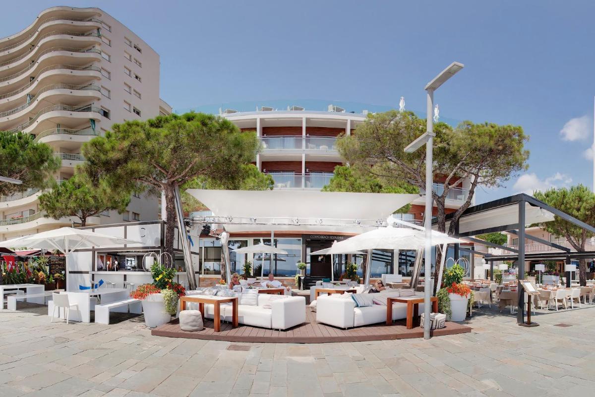 Un patio con mesas y sombrillas frente a un edificio. en Cosmopolita Hotel Boutique & Spa, en Platja d'Aro